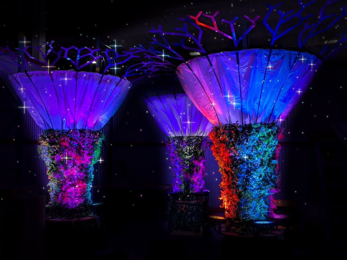 Glowing sculptural light trees in purple, blue and orange, sparkling in a dark venue
